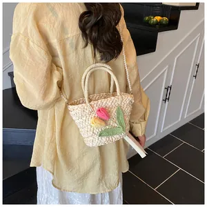 Detail of woven straw handbag with floral embroidery and pearl chain strap on a model