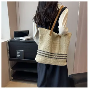 Detail of beige woven tote bag with black stripes and brown leather shoulder straps