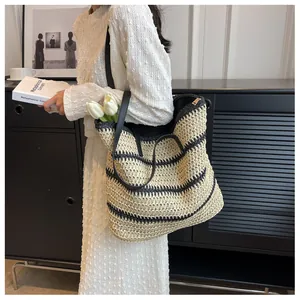 Close-up of woven straw tote bag with black stripes and leather straps on model shoulder
