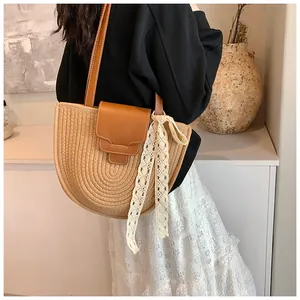 Détail du sac bandoulière en paille tressée avec lanière en cuir brun et nœud en dentelle