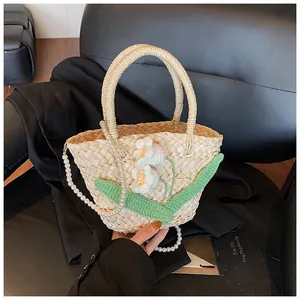 Detail of woven straw handbag featuring crochet flowers and white pearl chain strap