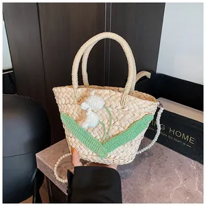 Detail of woven straw bag with knit flowers, green leaves, and pearl chain strap