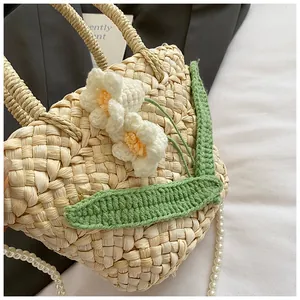 Detail of woven straw bag with white crochet flowers and elegant pearl chain strap