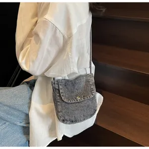 Detail of grey washed denim messenger bag featuring a flap closure and silver buckle