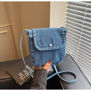 Detail of blue denim messenger bag with flap closure and silver metal snap button