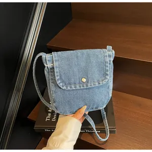 Detail of light blue denim crossbody bag featuring a silver metal button on flap cover