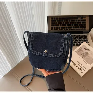 Detail of blue denim messenger bag showing white contrast stitching and silver metal buckle