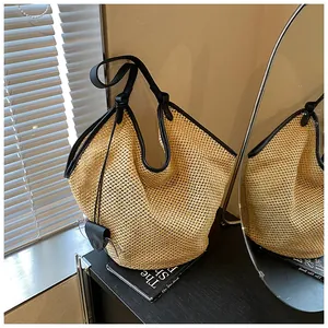 Detail of woven straw bucket bag with black faux leather trim and long shoulder strap