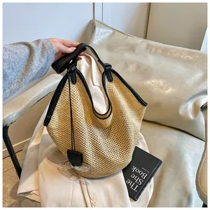 Detail of large straw tote bag featuring black leather handles and woven texture finish