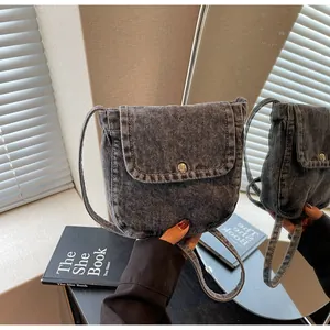 Detail of grey washed denim messenger bag featuring contrast stitching and flap closure