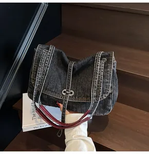 Detail of dark blue denim bag with contrast stitching and deep red leather handle wrap