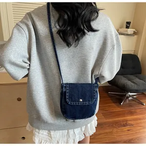 Detail of a navy denim crossbody bag with a metal snap button and visible stitching