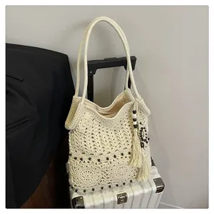 Detail of hollow-out woven tote bag with wooden beads and tassels on a white suitcase