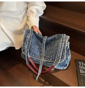 Detail of dark blue denim bag with white stitching and reddish brown leather handle