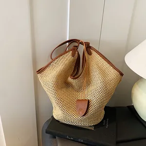 Detailed view of straw woven tote bag with brown leather trim and hanging teardrop charm