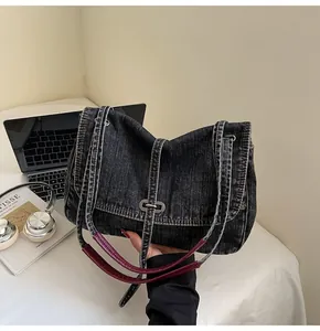 Detail of dark wash denim bag featuring burgundy leather handle and silver metal buckle