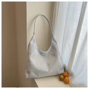 Close-up of a blue Hobo bag with bamboo and butterfly embroidery on a minimalist table
