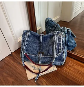 Detail of vintage denim shoulder bag with red leather strap on a wooden floor