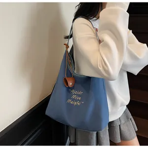 Détail du sac cabas bleu en toile avec petit charm en cuir marron sur la bandoulière