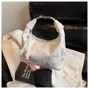 Detailed view of cream leather dumpling bag featuring silver butterfly and rhinestone accents