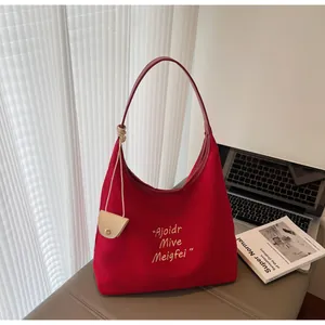Détail d'un sac cabas en toile rouge avec broderie jaune et breloque en cuir