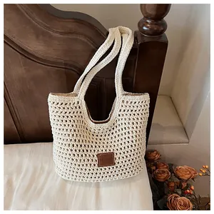 Close-up of cream woven crochet tote bag with brown leather logo patch on white bedding