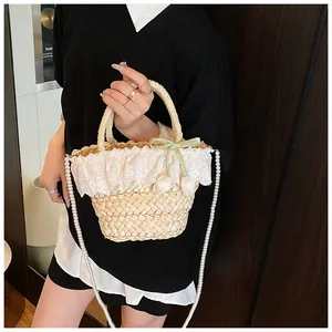 Détail d'un sac en paille avec bordure en dentelle blanche et bandoulière en perles