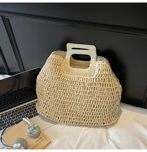 Close-up of a handwoven straw handbag with rectangular wooden handle on a desk