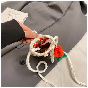 Detail of hand-crocheted white bag with floral pattern and orange fruit pendant