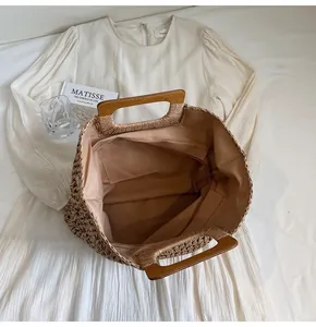 Detail of woven straw tote bag featuring wooden handles and brown fabric lining