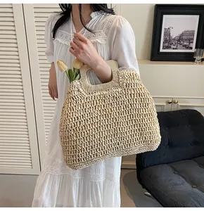 Detail showing the woven texture and wooden round handles of a beige straw tote bag