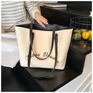 Close-up of cream canvas tote bag featuring black cursive embroidery and long straps
