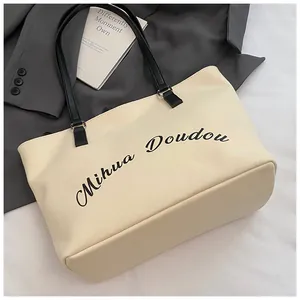 Detail shot of ivory canvas tote with chic black leather straps and artistic lettering