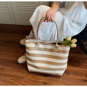 Detailed close-up of woven straw tote bag with wide khaki and white stripes and sturdy handles