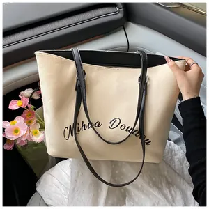 Close-up of beige tote bag with black trim and elegant cursive letter print inside a car