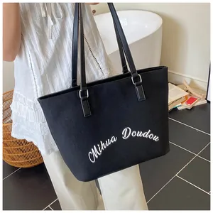 Detail of minimalist black tote bag featuring letter print and silver metal buckles