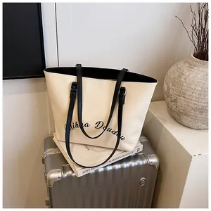 Close-up of large canvas tote bag with black letter print on silver suitcase