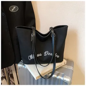 Detail of minimalist black canvas tote bag with white lettering and leather straps
