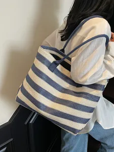 Large blue and white striped straw tote bag worn by model over shoulder on white background
