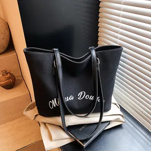 Macro shot of black canvas tote bag with white script print and leather straps