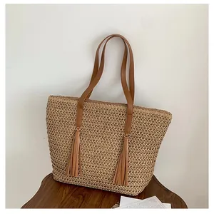 Detail der handgewebten beigen Strohtasche mit braunen Lederriemen und zwei Quasten
