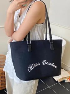 Minimalist black canvas tote bag with letter print shown on a model in a natural setting