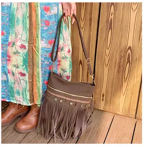 Detail of dark brown crossbody bag featuring long tassels and ethnic metal charms on texture