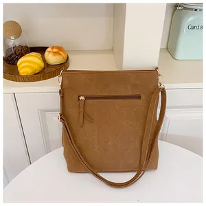 Detailed back view of brown suede shoulder bag featuring a zipper pocket and gold hardware