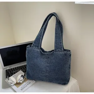 Detail view of large navy blue washed denim tote bag next to laptop on desk