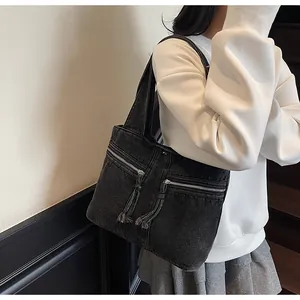 Detail of black denim tote bag featuring dual zipper pockets and fringe tassel pullers
