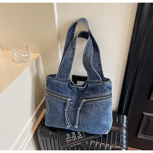 Close-up of blue denim tote bag with zipper pockets resting on black suitcase