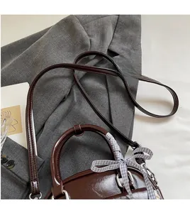Détail du sac en cuir bordeaux avec bandoulière réglable et ruban posé sur un blazer