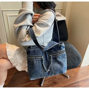Detail of blue denim tote bag with zipper pockets worn as casual crossbody bag