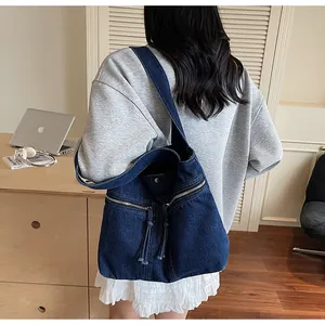 Detail of dark blue denim tote bag with dual front zippers and snap closure on a model